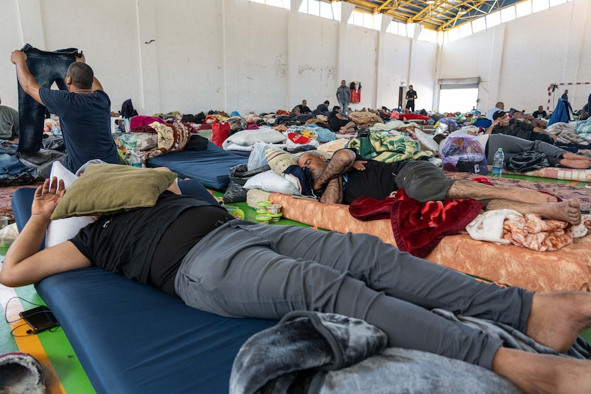 Men lay down on makeshift beds inside a large warehouse type room