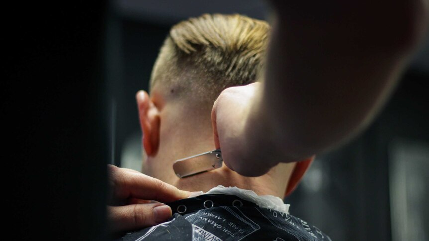A barber uses a razor to shave the back of a man's head.