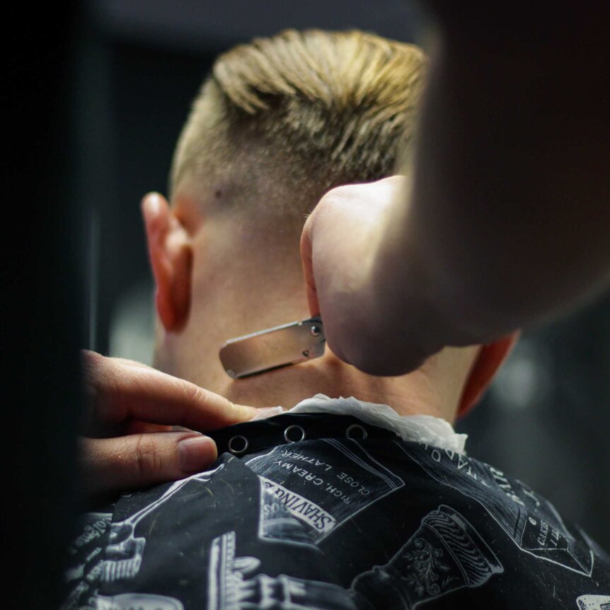 A barber uses a razor to shave the back of a man's head.