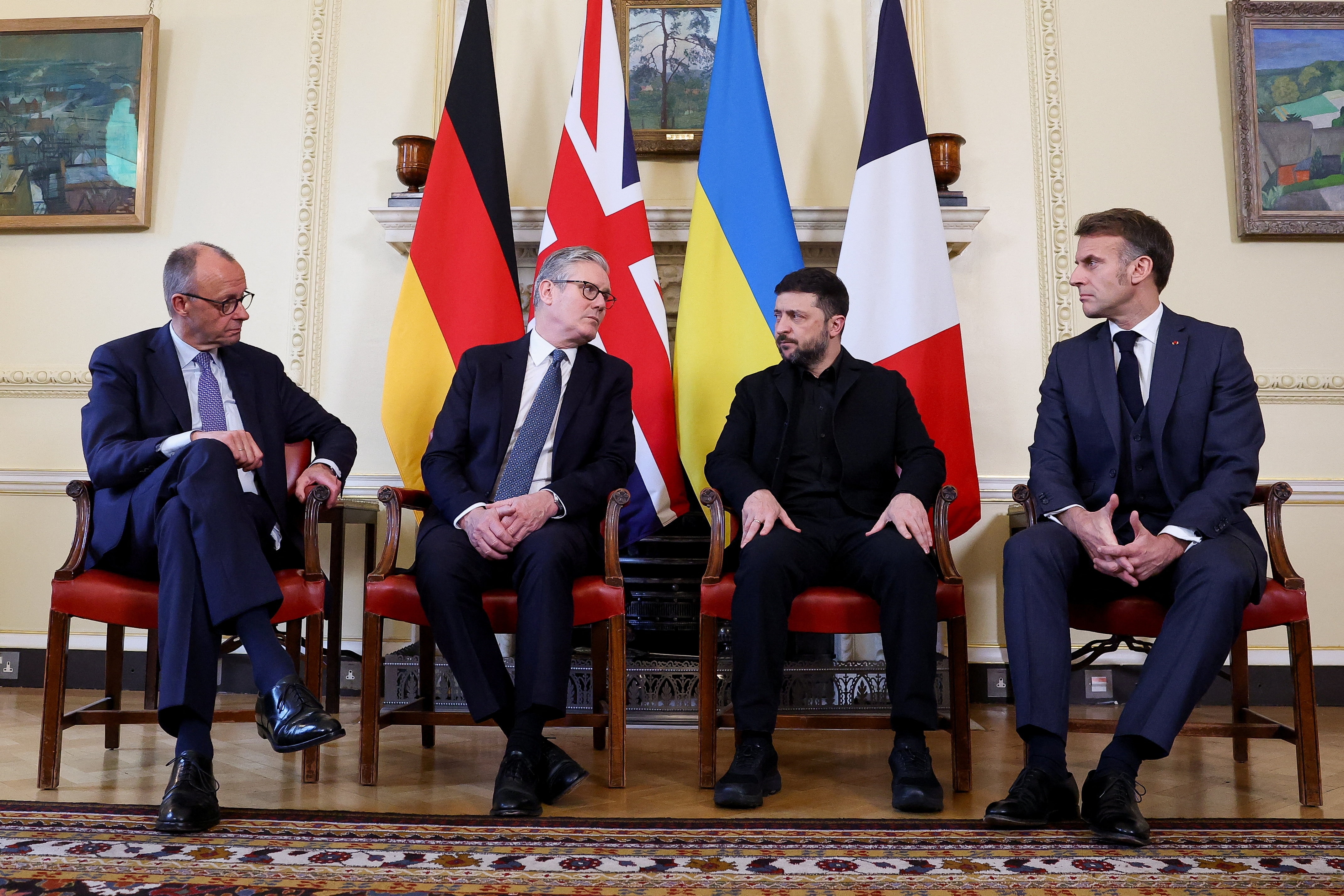 Four men sit on chairs in front of several nations' flags in a room at 10 Downing Street.
