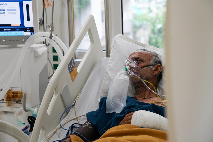An elderly Indian man with an oxygen mask on his face