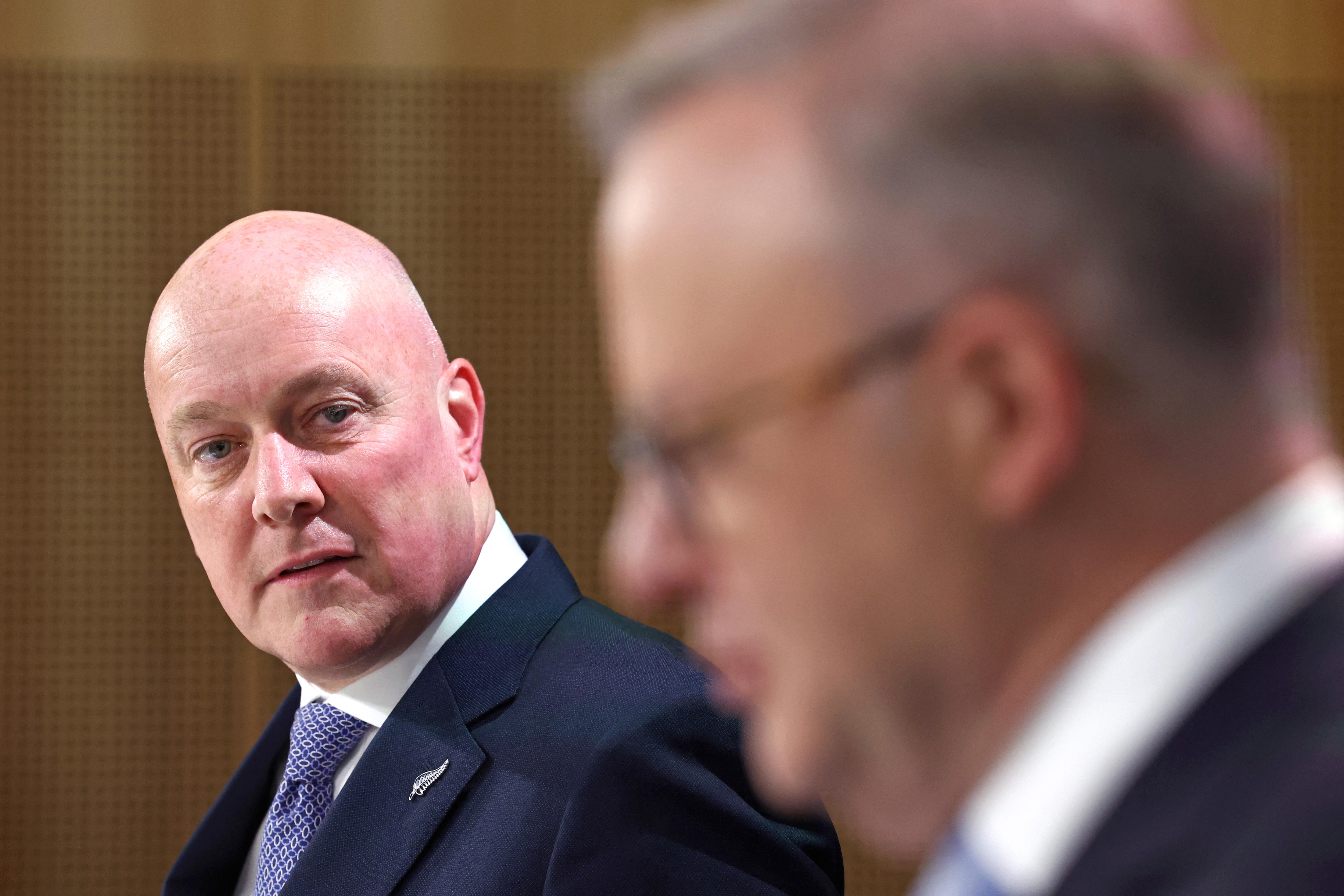 New Zealand's prime minister Christopher Luxon listens while Anthony Albanese (out of focus in the foreground) speaks.
