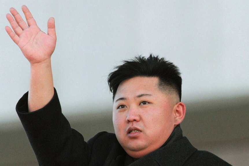 North Korean leader Kim Jong-un waves with his right hand while wearing a thick grey military-style coat