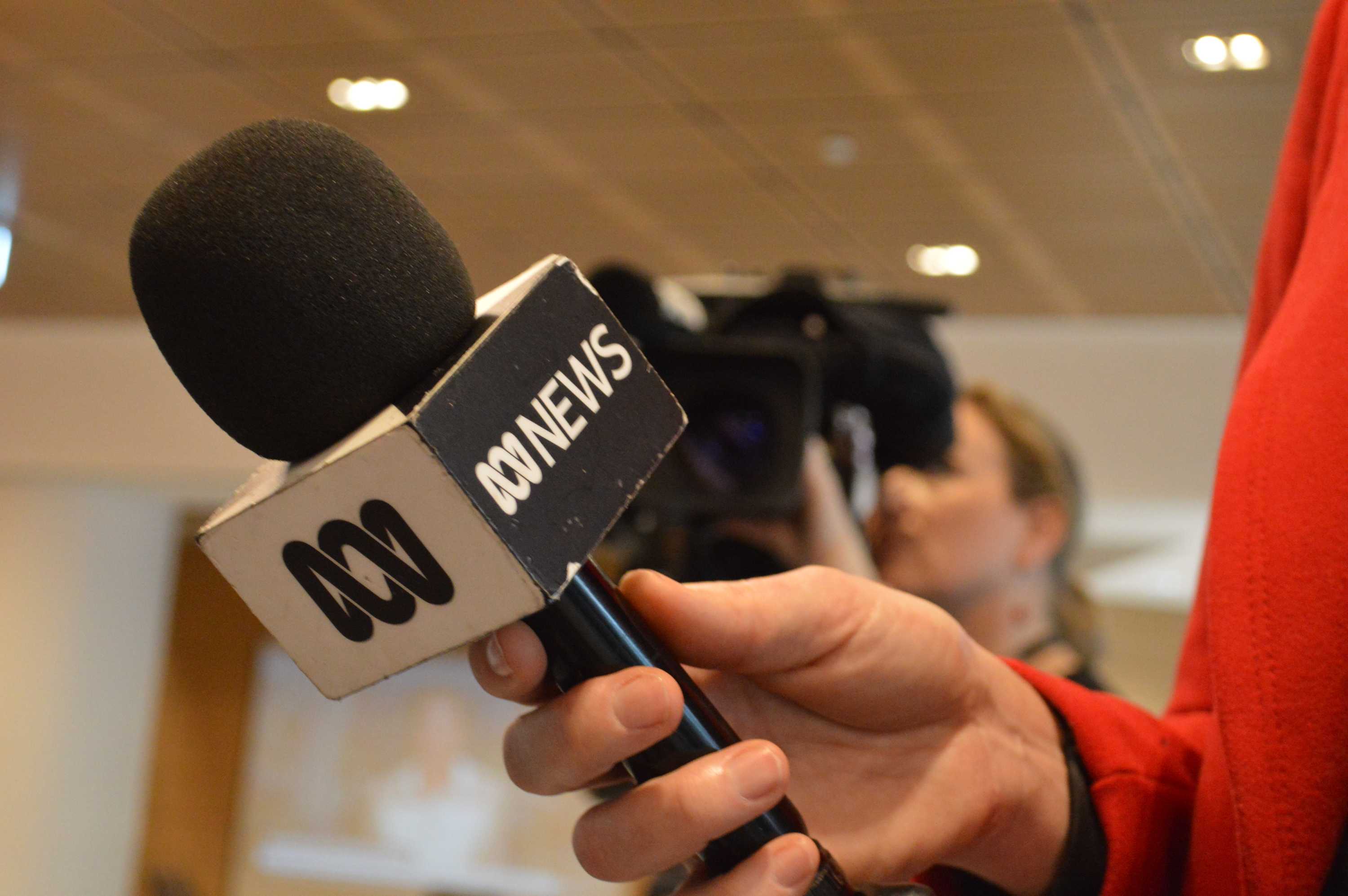 Close up of microphone with ABC News logo in hand with camera in the background.