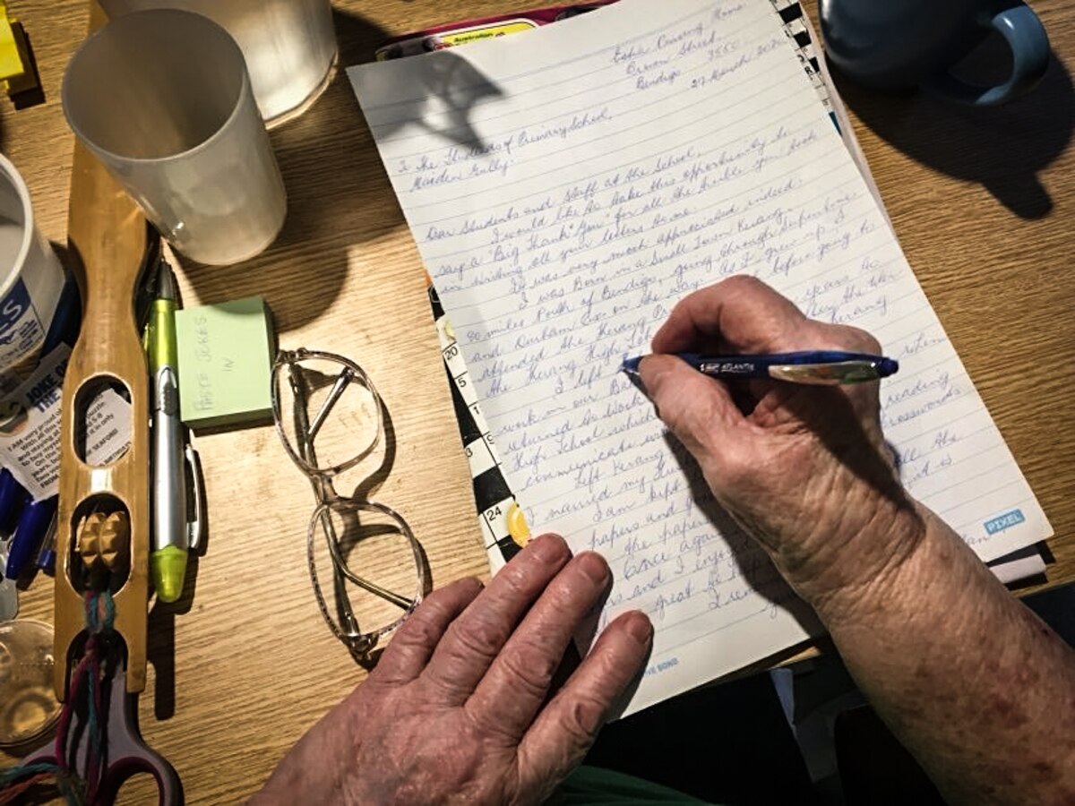 An older person&#x27;s hands holding a pen and writing a letter.