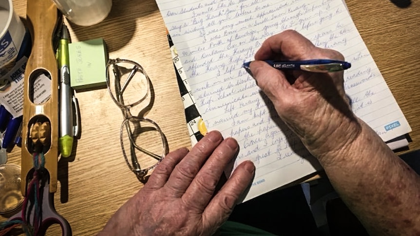 An older person's hands holding a pen and writing a letter.