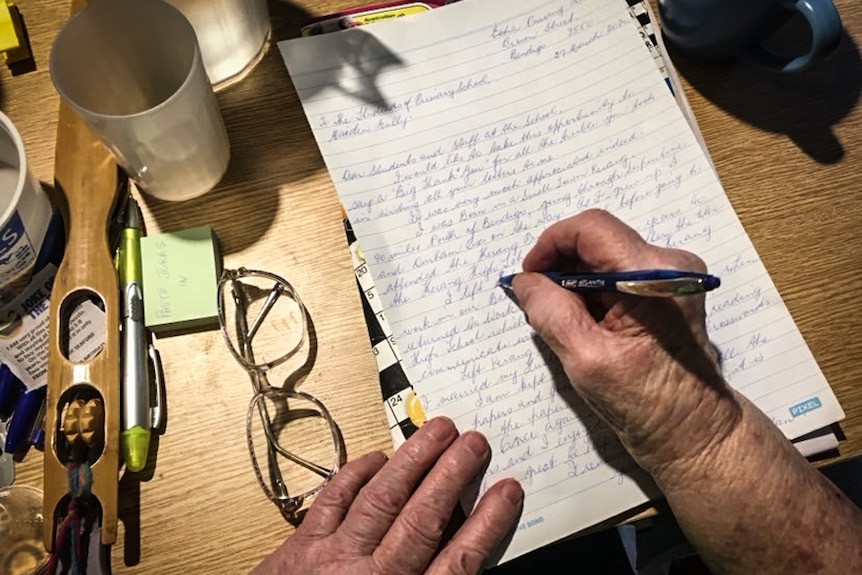 An older person's hands holding a pen and writing a letter.