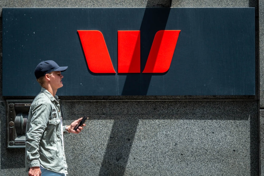 A man holding his mobile phone walks past a Westpac Bank sign in George street Sydney on January 28 2019.