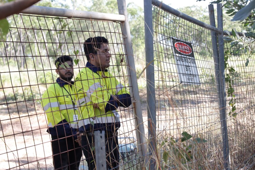 two tradies stand behind a wire mesh fence