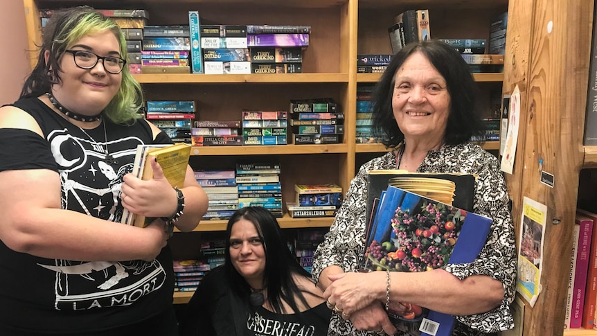 Three ladies holding onto books near a book shelf.