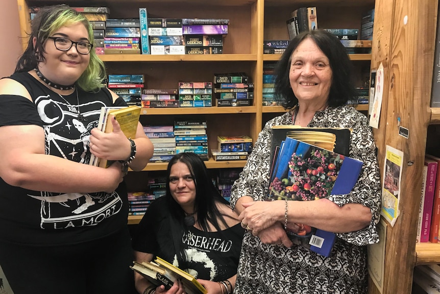 Three ladies holding onto books near a book shelf.