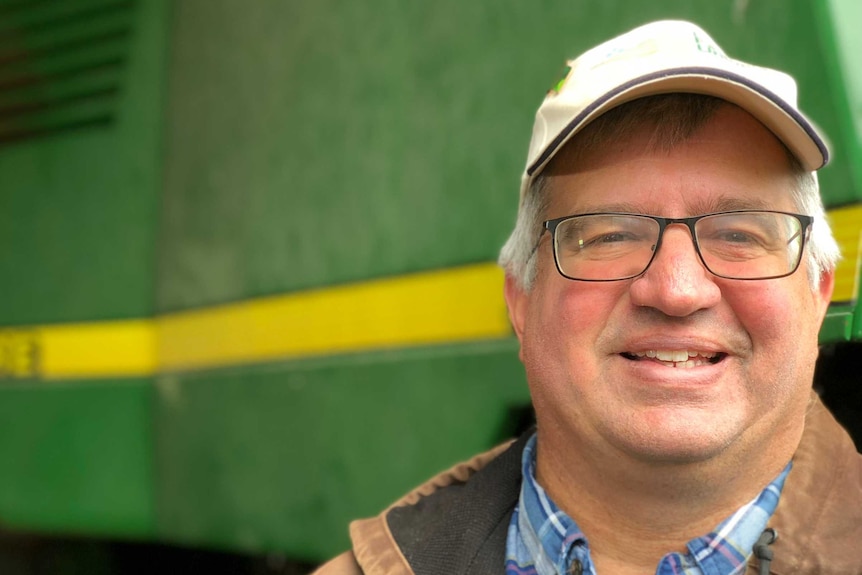 Farmer Aaron Lehman smiles in front of farm equipment.