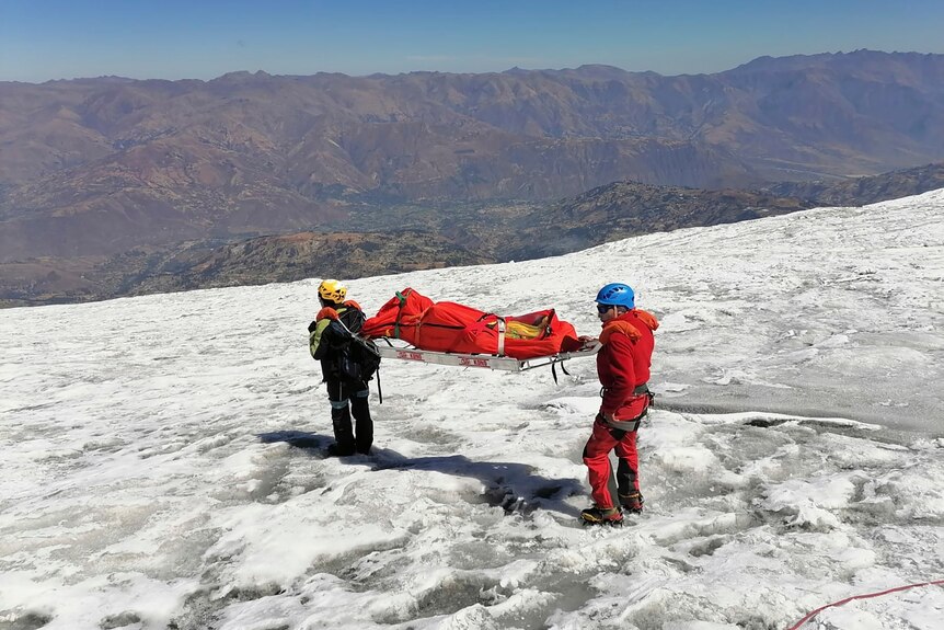 Mountain rescue stand on snowy peak with body on stretcher 