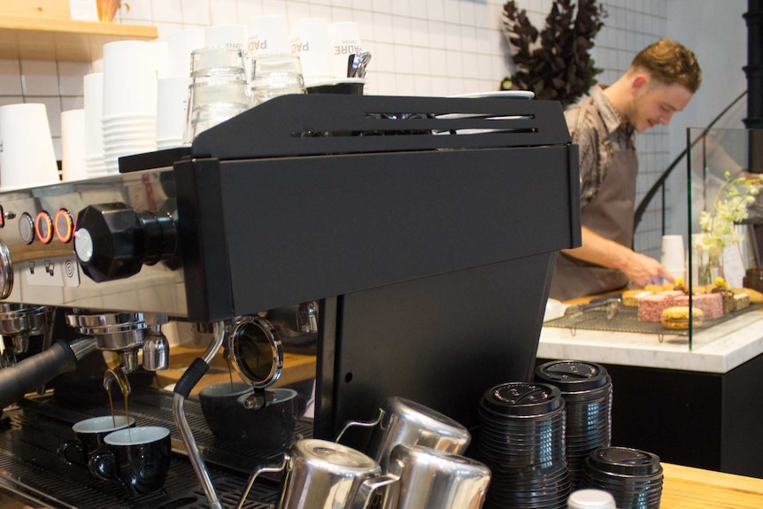 A commercial coffee machine, worker at counter.