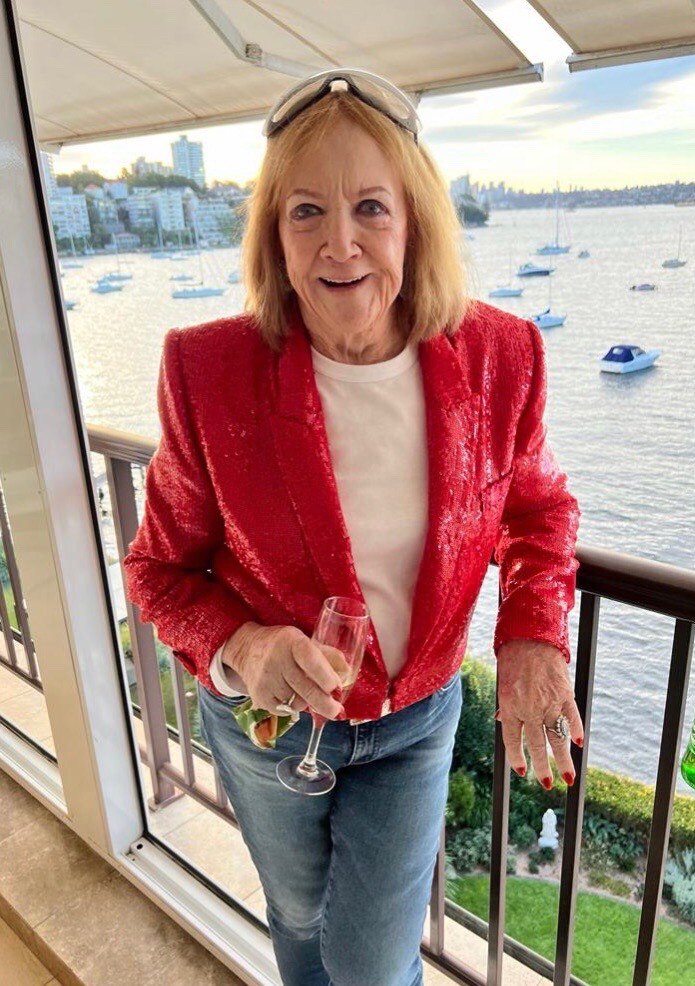 Eileen Bond smiles at the camera by the river, wearing a red jacket.