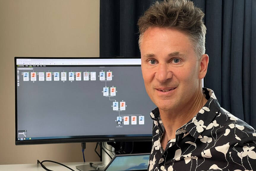 man wering a collared shirt sits in front of a computer showing a family tree