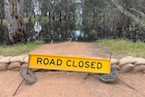 A 'road closed' sign near a flooded river.