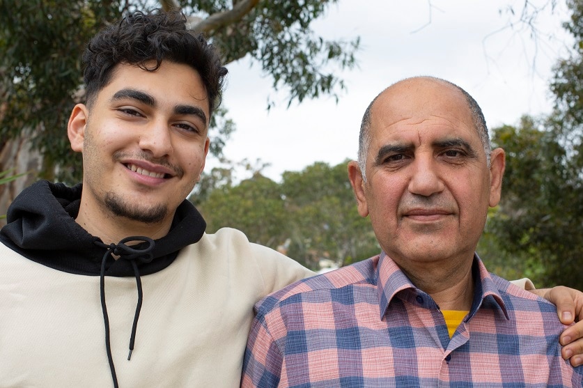 A young man put his arm around an older man and smiles