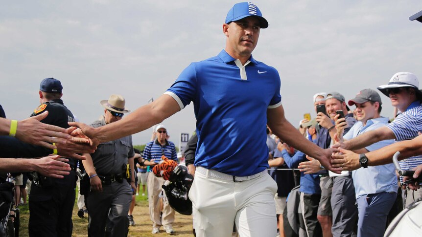 A golfer spreads his hands out to catch spectators as he walks through a crowd.