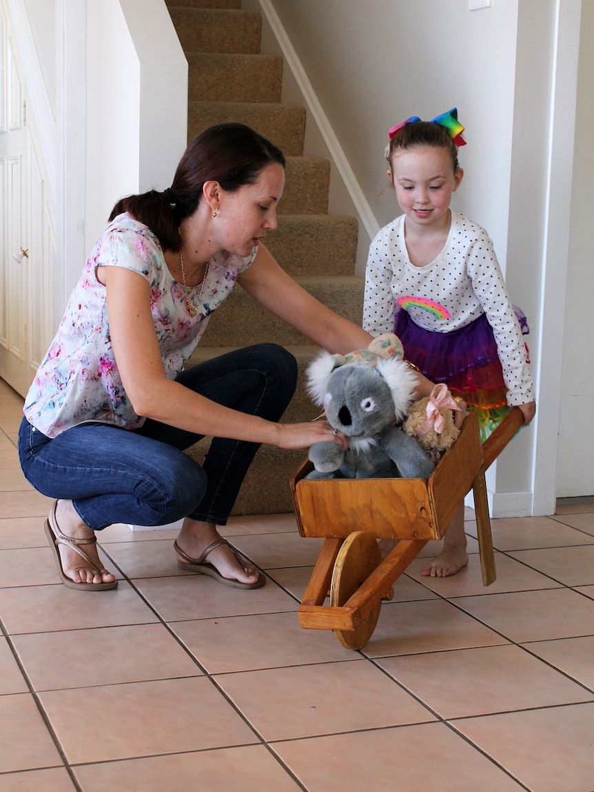 Hayley Ryan plays with her teddies in a wheelbarrow with her mother Melissa in their lounge room.