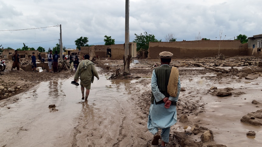 Image of two men walking away from the camera, the ground looks muddy and wet.