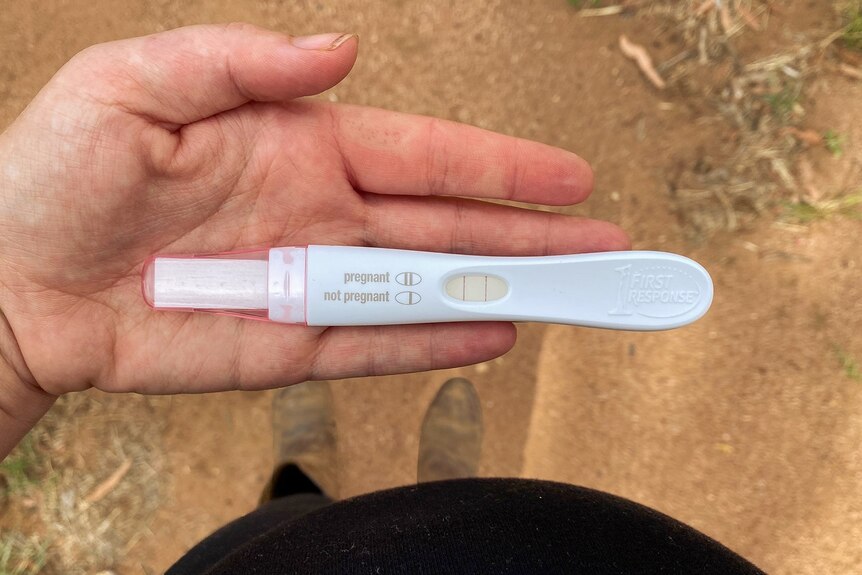 pregnant woman holds a positive pregnancy test on a dirt road
