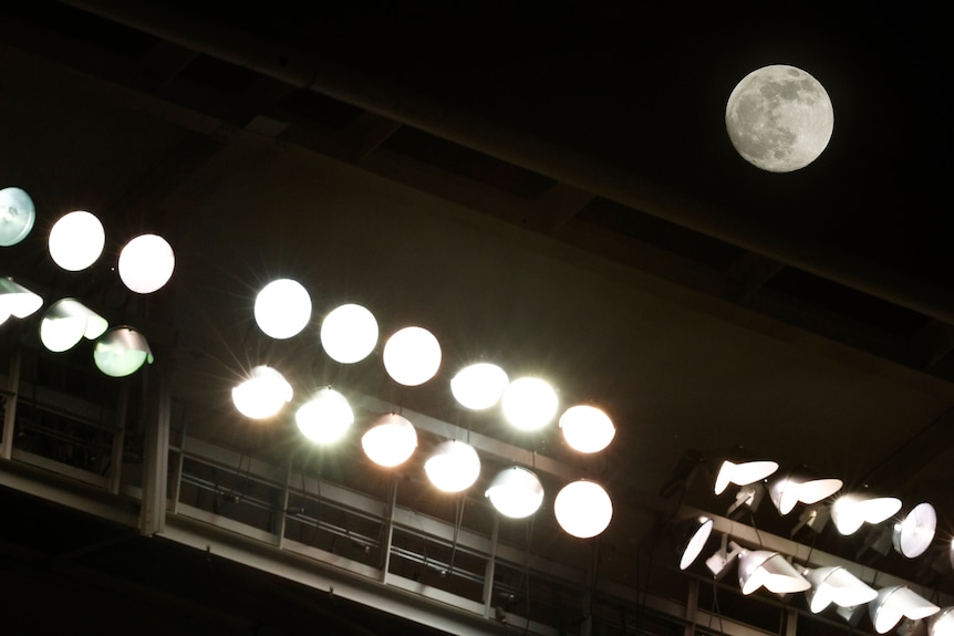 A full moon above stadium lights.
