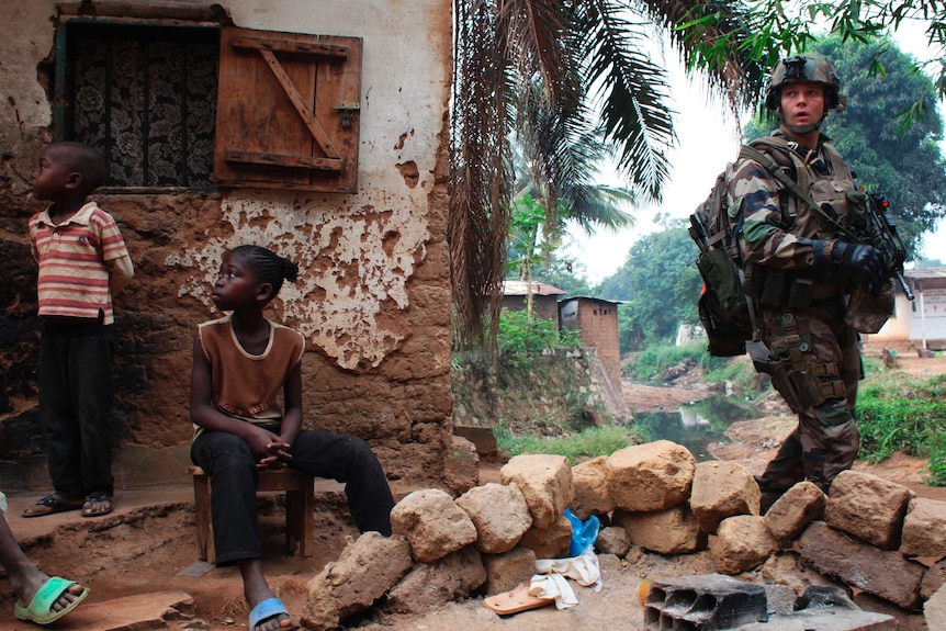 A soldier walks past two African children.