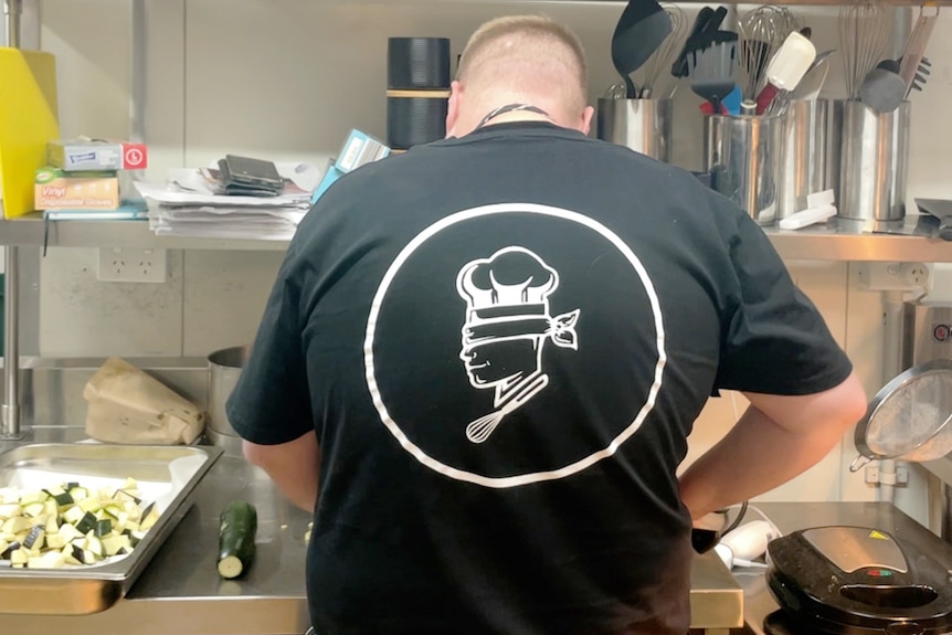 The back of a man's black t-shirt which has on it a white drawing of a chef wearing a blindfold
