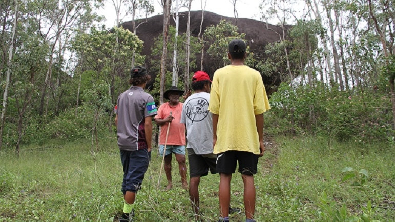 Indigenous elder Russell Butler stands with three young people in front of Turtle Rock, a sacred site in north Queensland