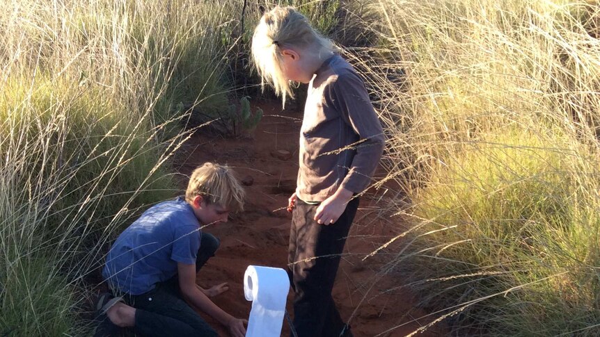 Two young boys digging in red soil among high grass