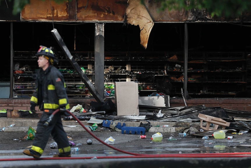 Firefighters walk out the front of a burned out shell of a building.