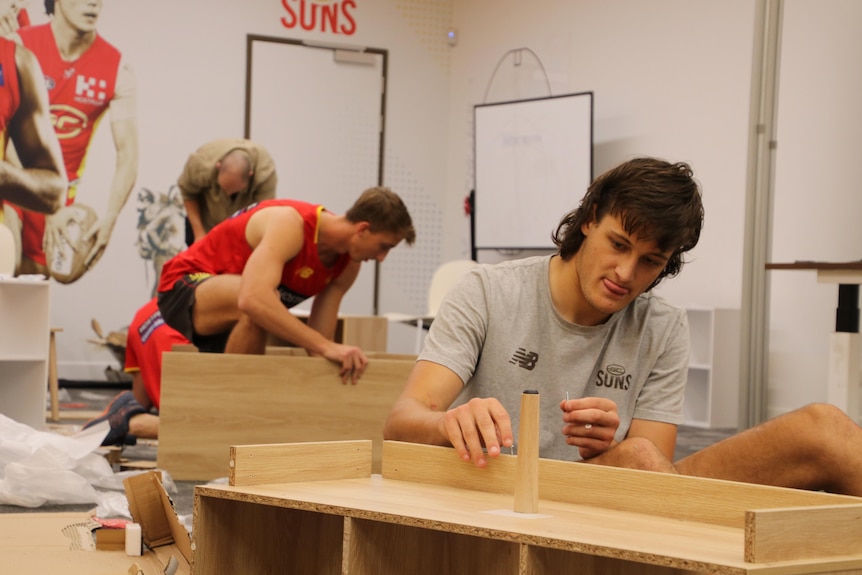 Gold Coast Suns players assemble furniture that they donated to DV organization RizeUp.