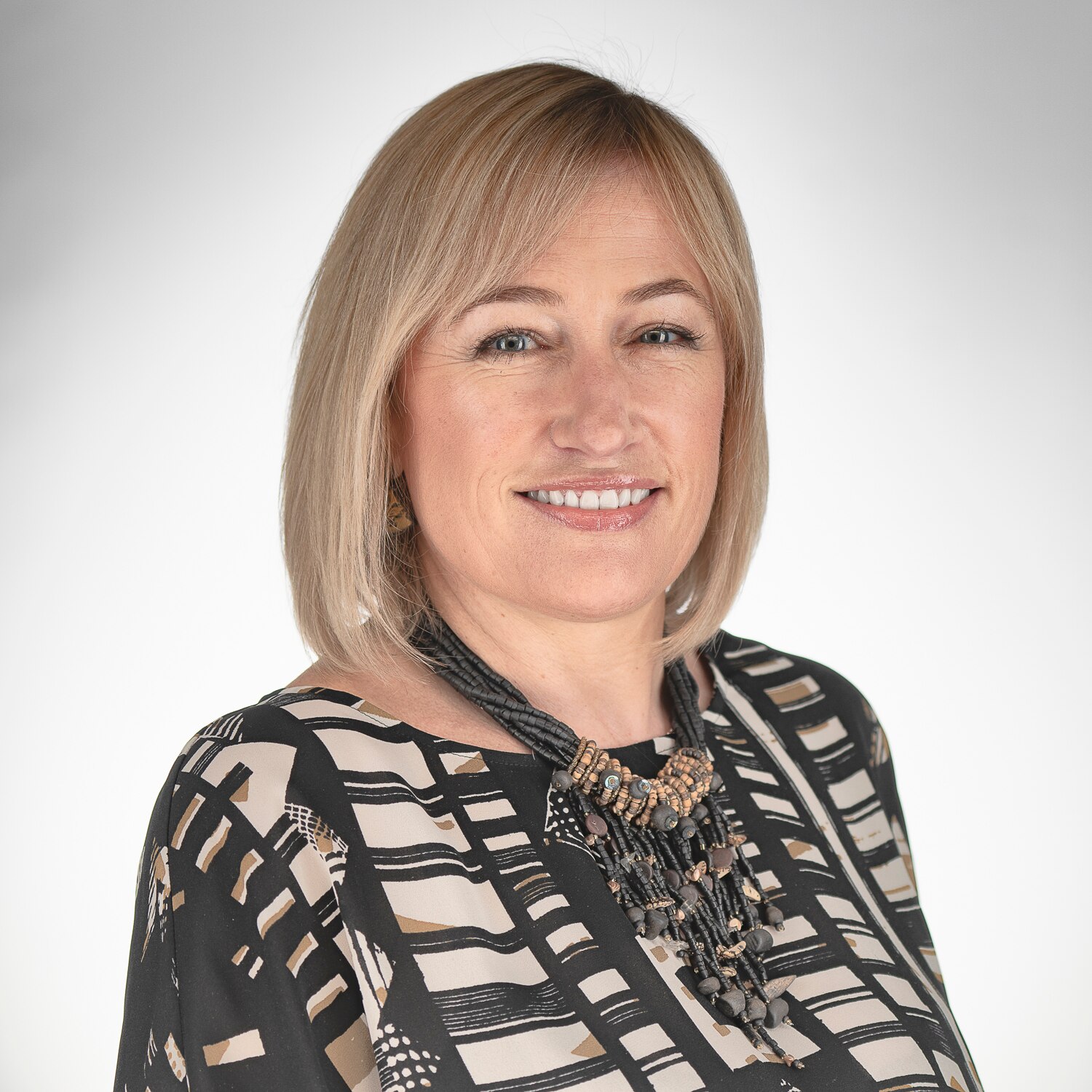 Portrait of Anna Bunn who is smiling at the camera. She has shoulder length blond hair and is wearing a black and white shirt.