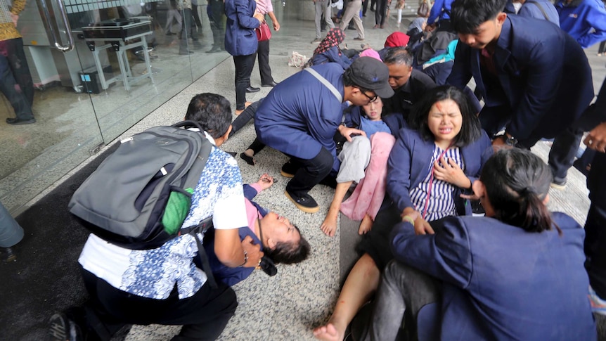 Injured people on the ground outside the Indonesia Stock Exchange, with people helping them.