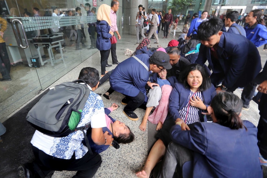 Injured people on the ground outside the Indonesia Stock Exchange, with people helping them.