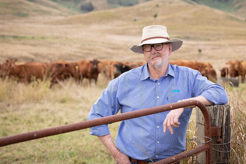 Farmer and melanoma survivor standing by a gate with cattle in the background