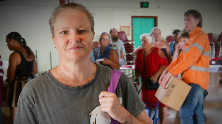 A woman holding a bag on her shoulder looking at the camera, in front of a queue of people