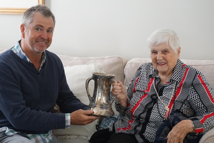 man sitting on couch next to elderly woman both holding silver cup