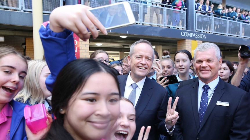 Bill Shorten offers double high fives as he's surrounded by a crowd of school students