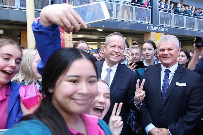 Bill Shorten offers double high fives as he's surrounded by a crowd of school students