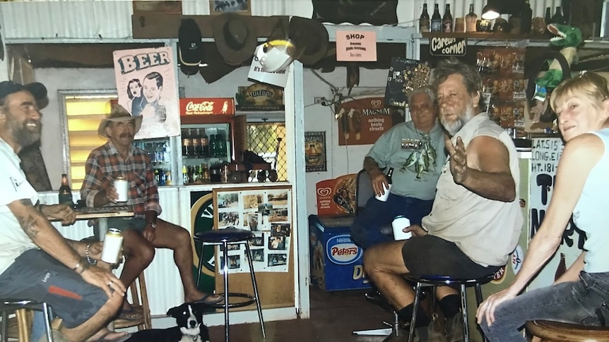 Five people sit around an outback pub drinking stubbies of beer held in coolers.