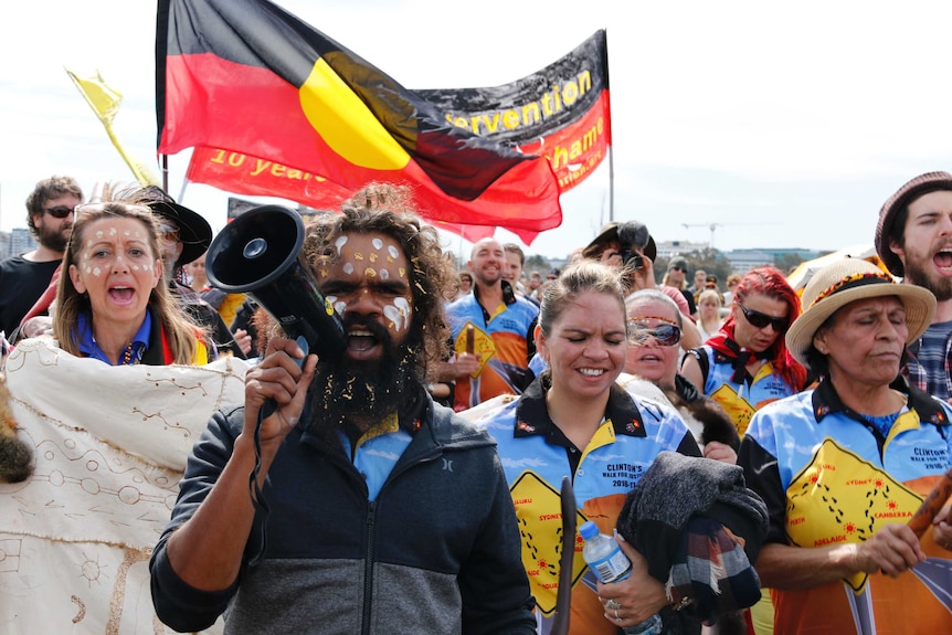 Clinton Pryor walks with supporters holding banners and Aboriginal flags.