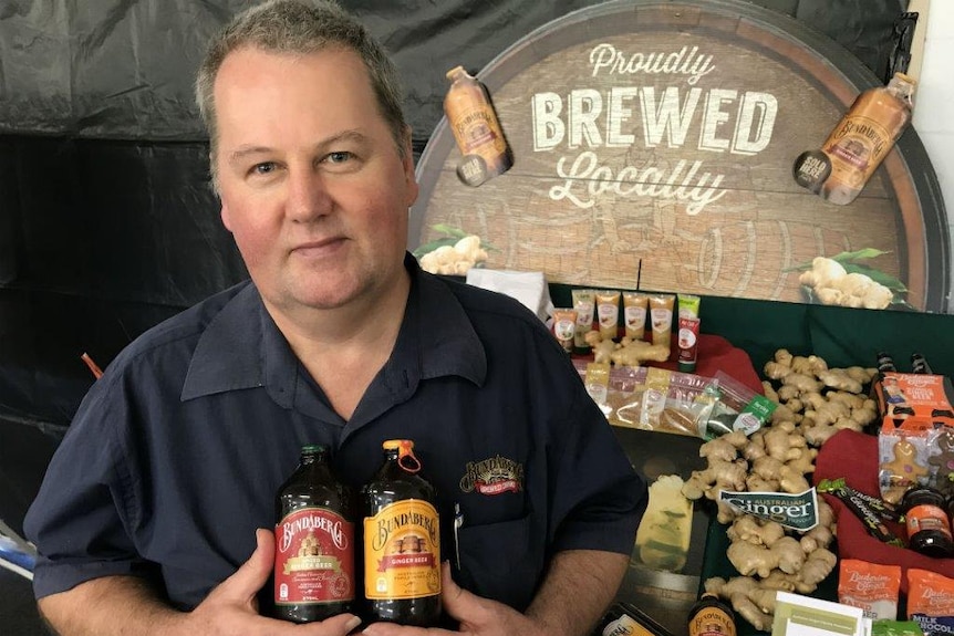 David Andrews stands in front of a stand displaying his drinks and other products made from ginger.