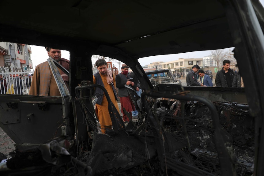 People look at the inside of a car that  has been burned out by the blast. The interior is completely blackened.