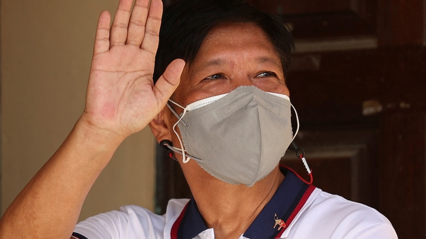 A man wearing a face mask waves to supporters