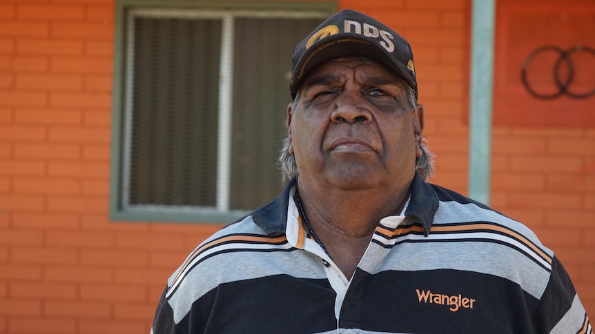 An Aboriginal man wearing a cap and a black, grey and orange striped shirt.