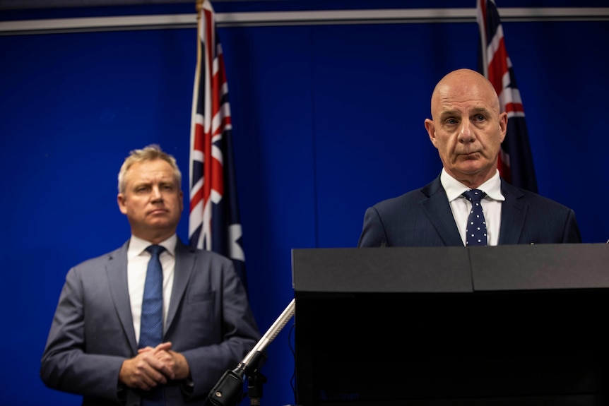 Two men in suits stand next to a flag