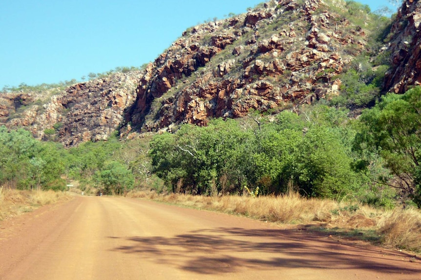 The Gibb River Road surrounded by trees and rocky hills.