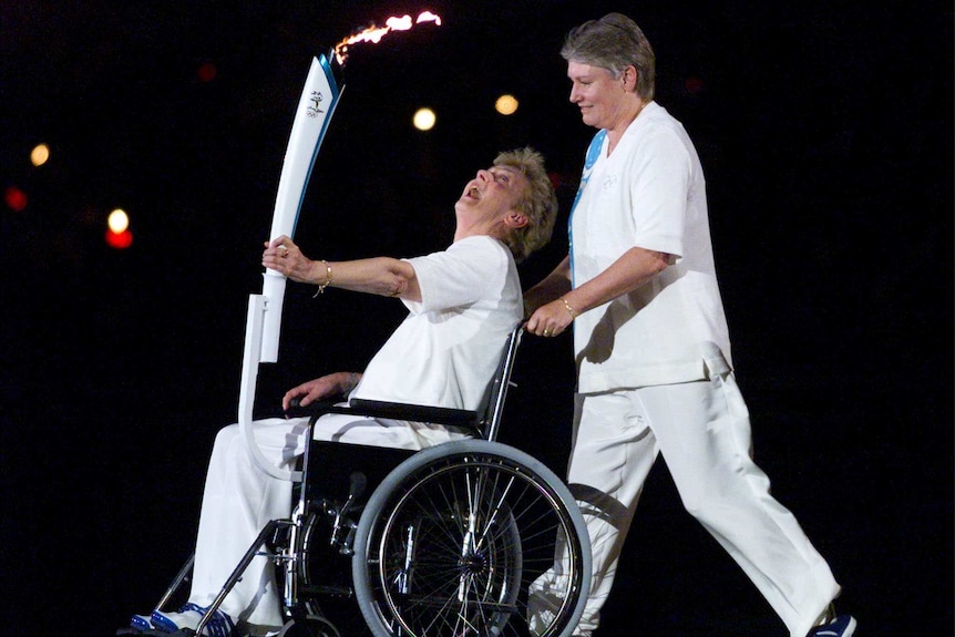 Betty Cuthbert in a wheelchair being pushed by Raelene Boyle while wearing white at Sydney 2000 Olympic Games opening ceremony